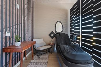 A black massage bed sits in a room with a wooden table and a chair.